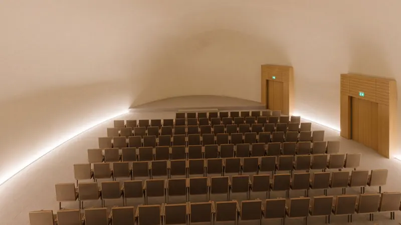 Vista 3D del salón terminado: patio de butacas bajo el ovoide acústico, con la luz rasante de la escocia. Render del modelo con acabado asistido por IA.